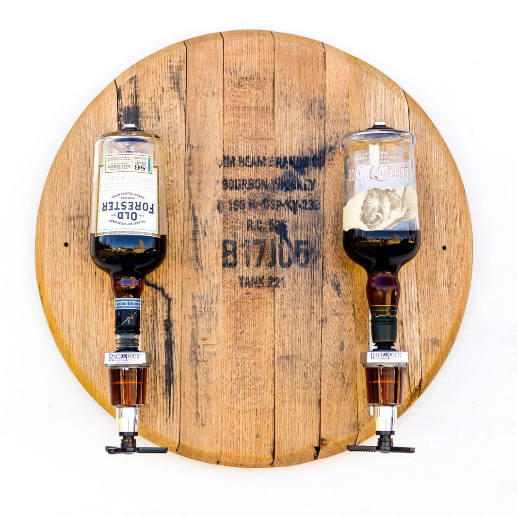 Two whiskey dispensers mounted on a wooden barrel head with two pouring spouts and a metallic mechanism.