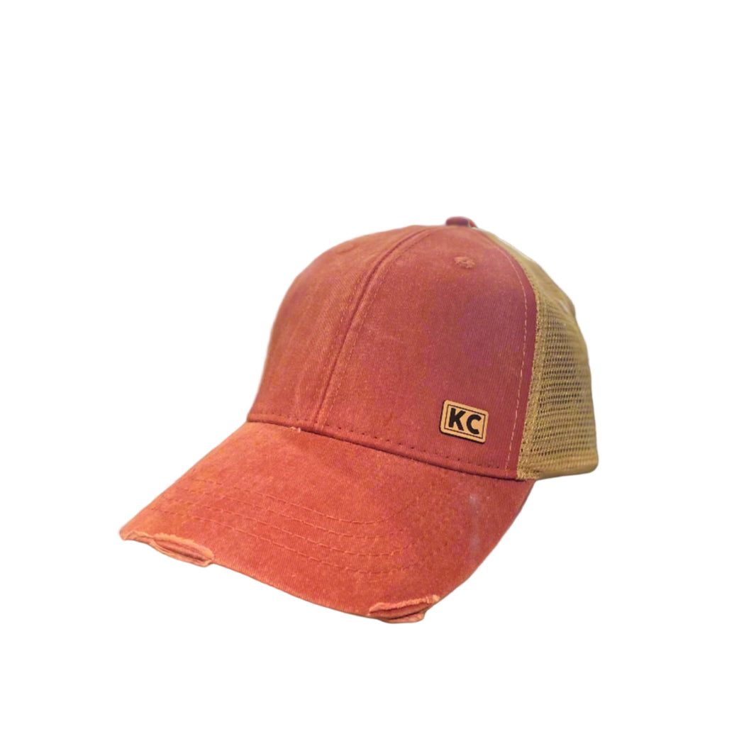 A red vintage-colored ball cap with a KC leather patch on the front.