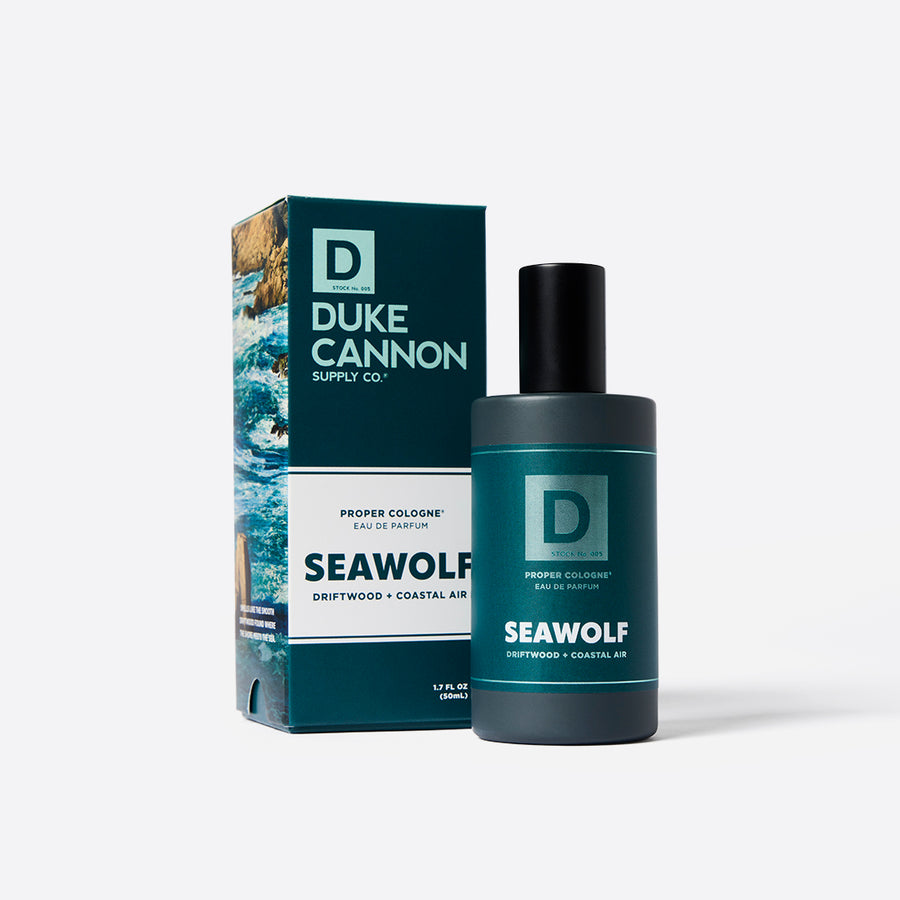 A product image featuring a bottle of Duke Cannon Proper Cologne - Seawolf next to its packaging box. The cologne bottle is dark blue with a black cap, and the box has a blue and green design with text and wave graphics.