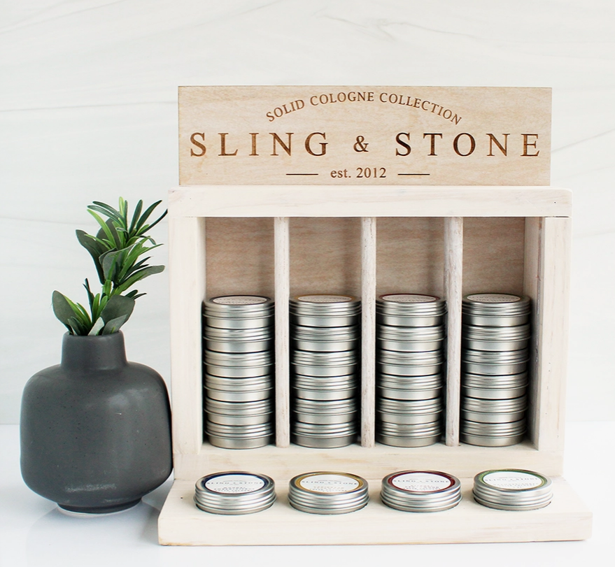 A display assortment of Sling & Stone solid cologne tins beside a plant in a black stone vase.