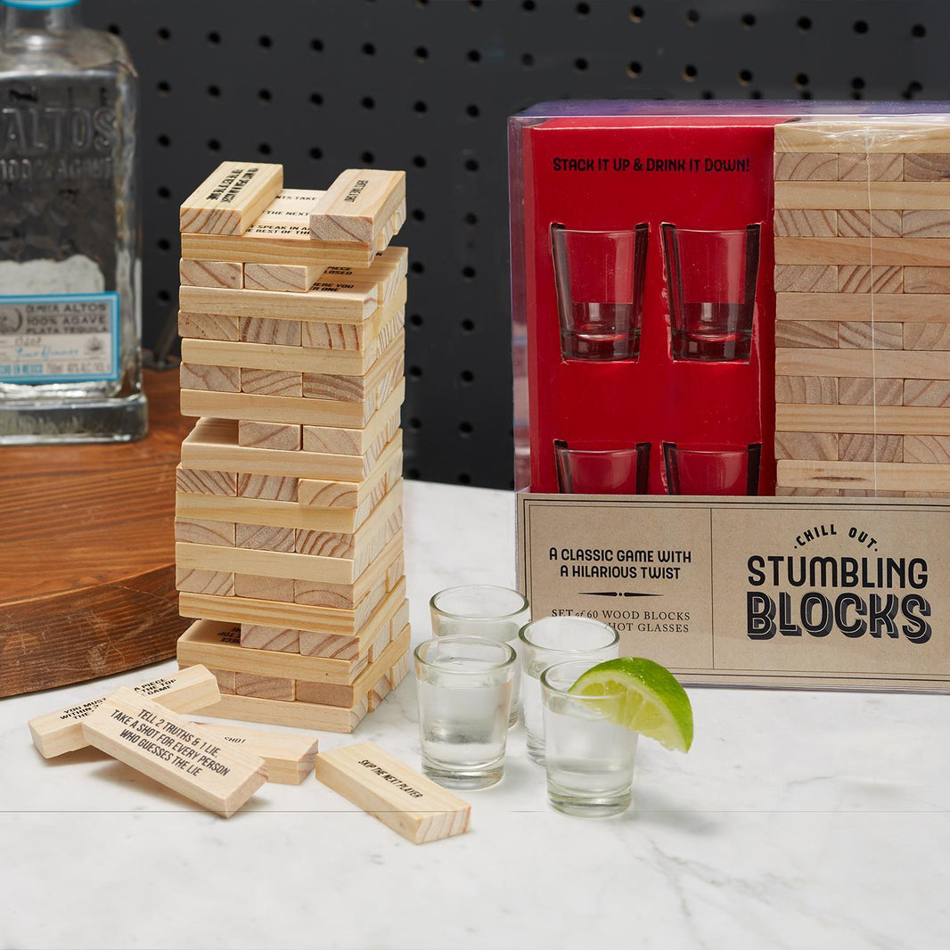 The image shows a drinking game called Stumbling Blocks with Shot Gasses, which includes wooden blocks with sayings, blank blocks, and four shot glasses, all packaged in a red gift box.