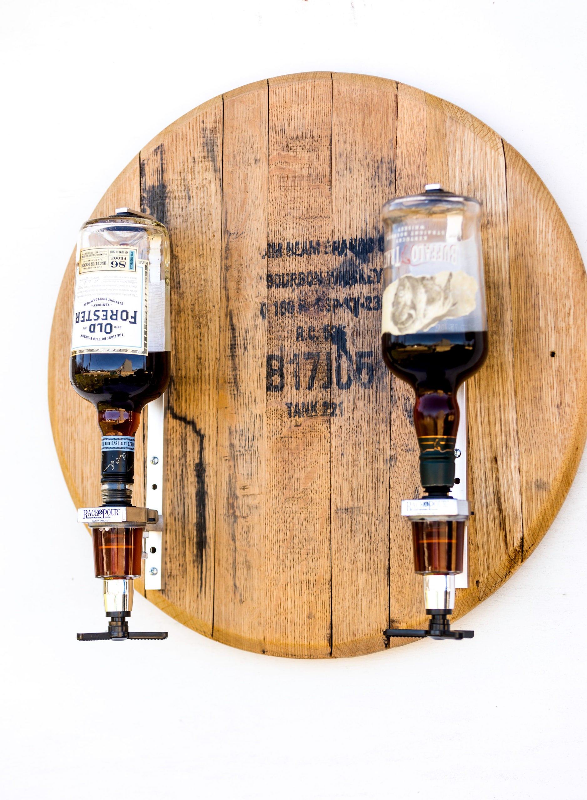 Two whiskey bottles mounted on dispensers that are attached to a barrel head on a white background.