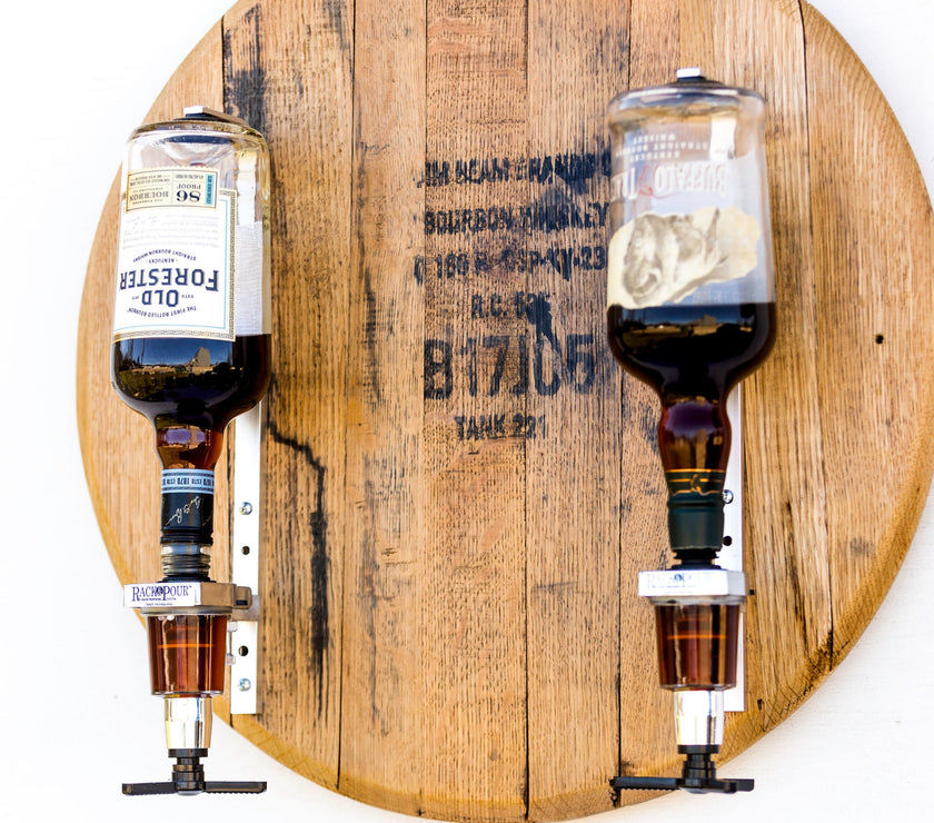 Two whiskey bottles mounted on dispensers that are attached to a barrel head on a white background.
