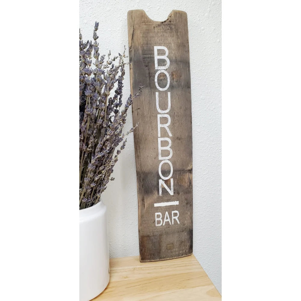 Wooden sign with 'Bourbon Bar' text next to a vase of lavender on a white background