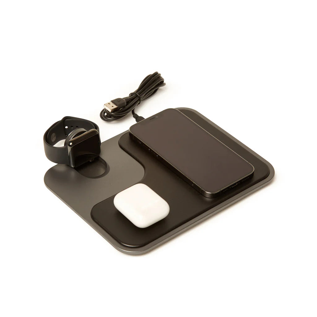 Black and gray wireless charger with a watch, phone, and earbud case on it, on a white background