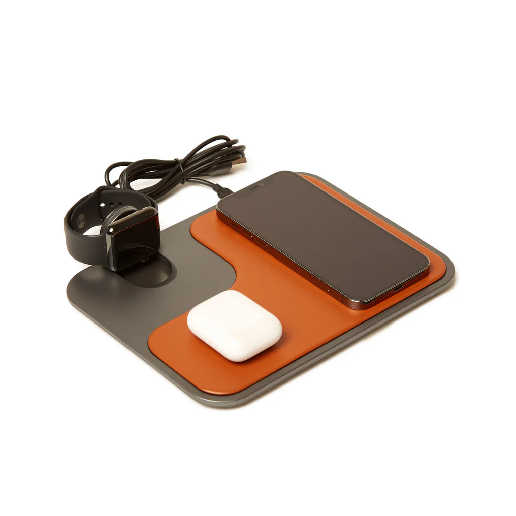 Brown and gray wireless charger with a watch, phone, and earbud case on it, on a white background