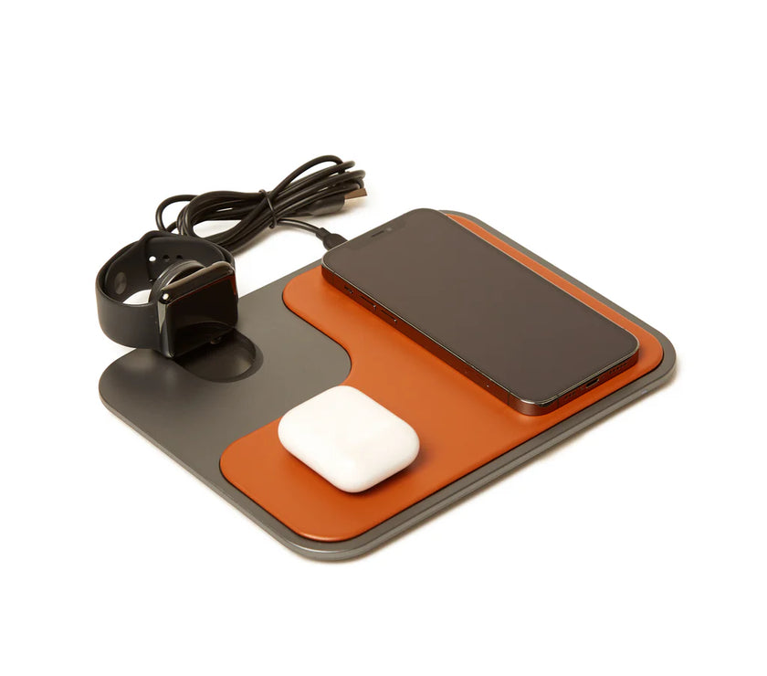 Brown and gray wireless charger with a watch, phone, and earbud case on it, on a white background