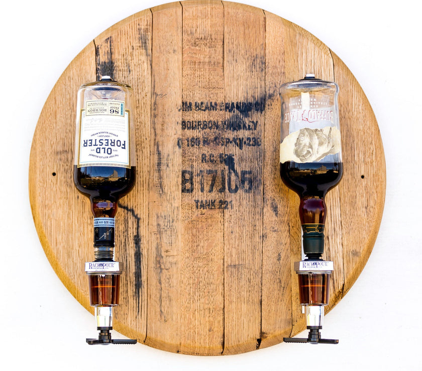 Two whiskey dispensers mounted on a wooden barrel head with two pouring spouts and a metallic mechanism.