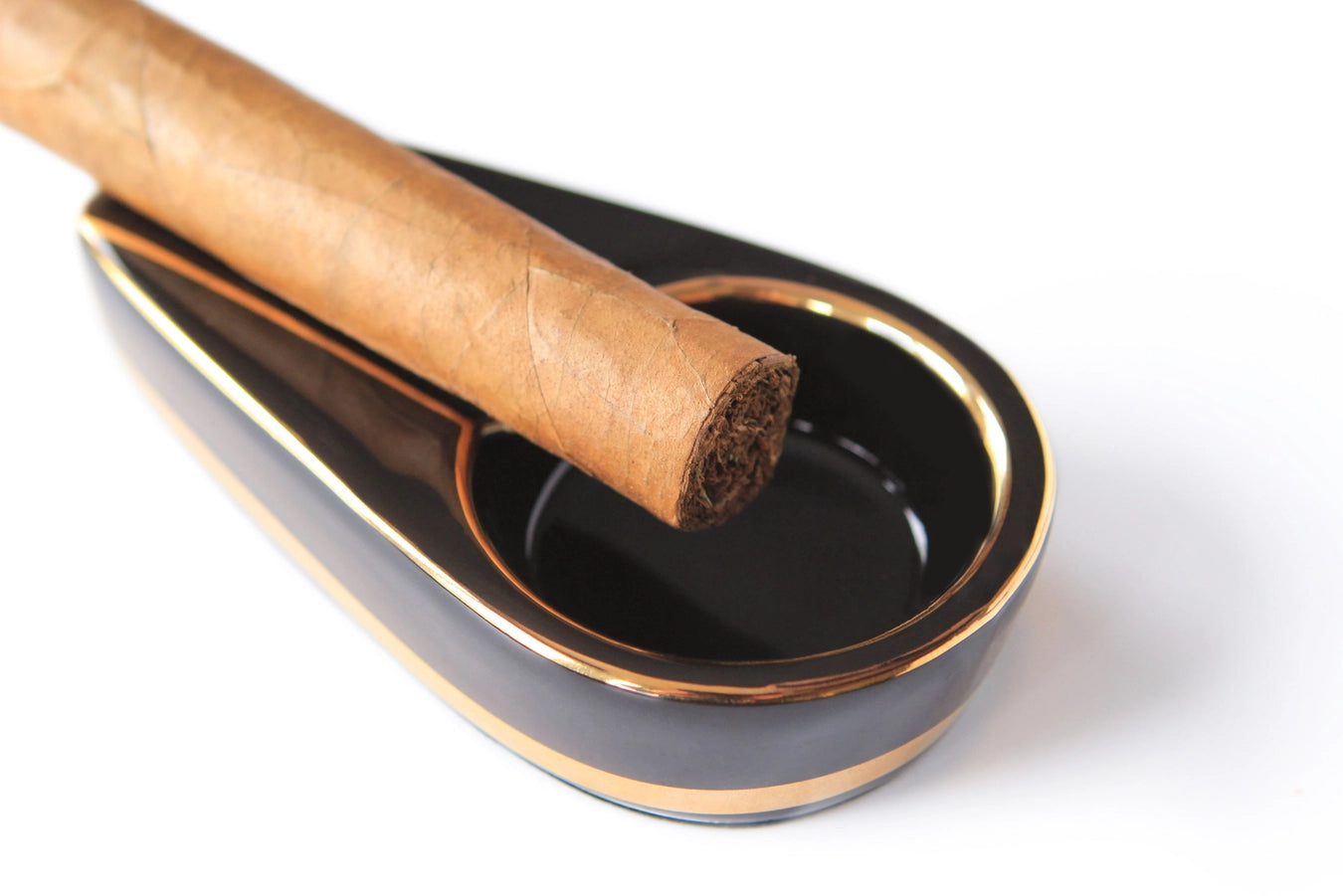 A closeup of the tip of a cigar resting in a brown and gold cigar ashtray.