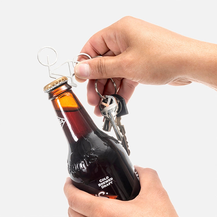Hand using a bottle opener on a bottle with keys attached, on a white background