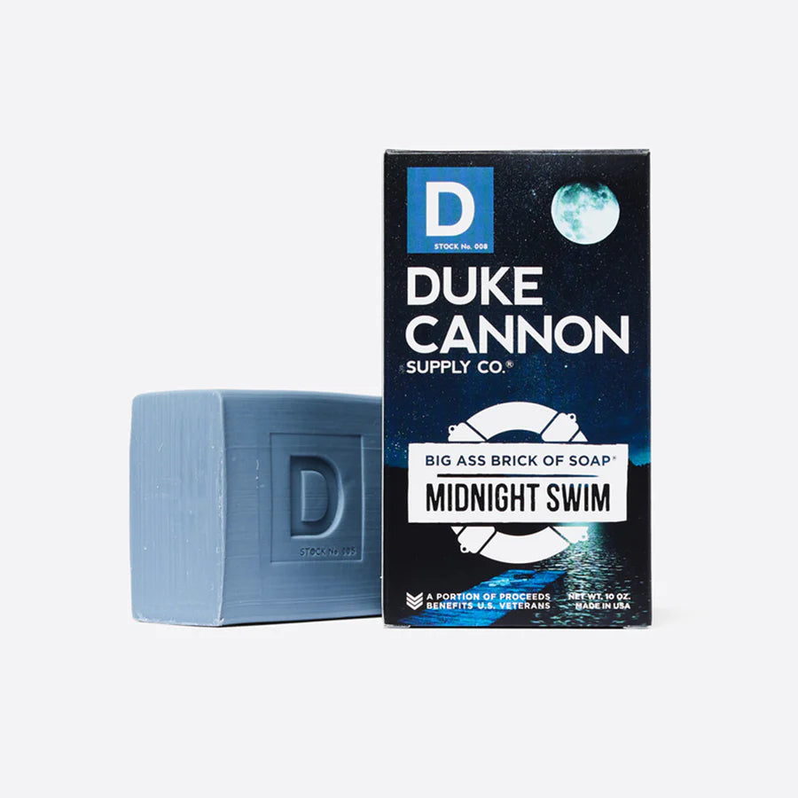A blue bar of soap next to its packaging box with 'Duke Cannon Supply Co.' and 'Midnight Swim' text on it.