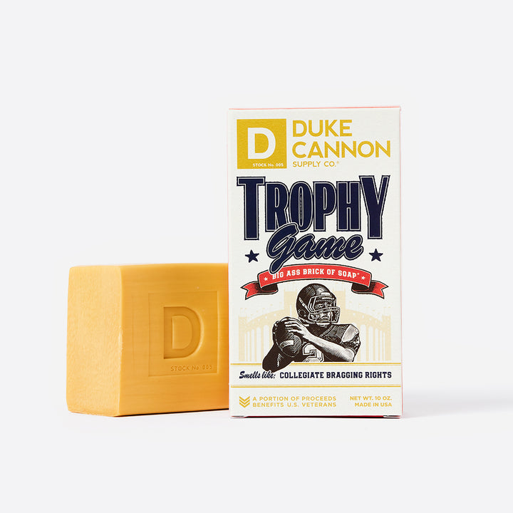 A 10 oz bar of soap next to its packaging box, which features the text 'Duke Cannon Trophy Game' and an image of a football helmet.