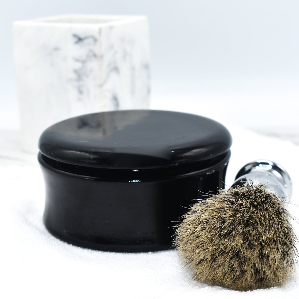 A black mango wood shave bowl next to a shaving brush on top of a white towel.