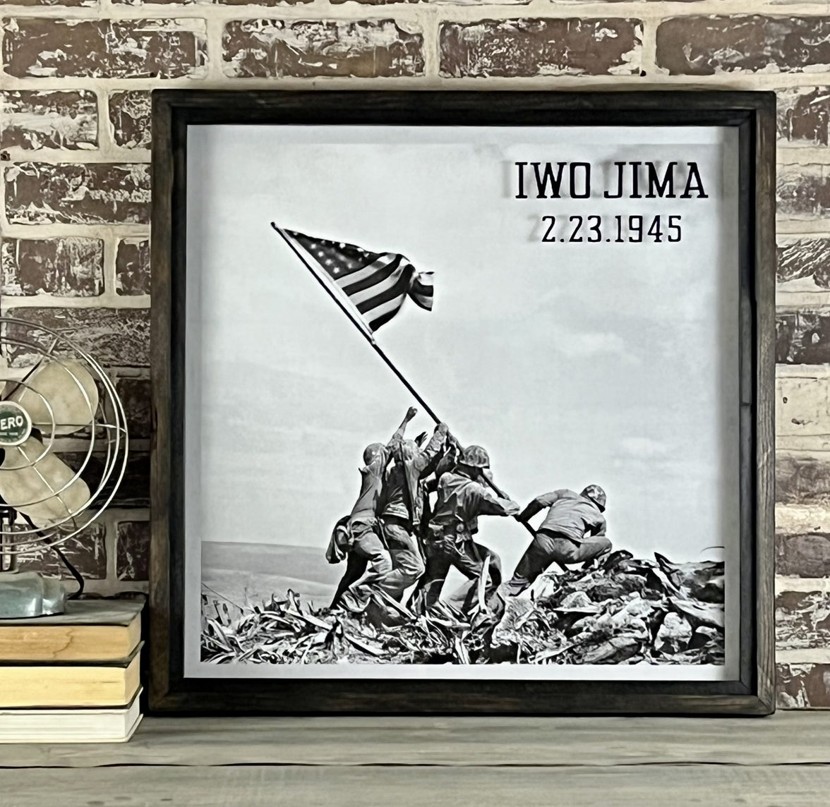 A framed artwork depicting the Iwo Jima flag raising, featuring an image of soldiers raising the American flag, with the text 'Iwo Jima 2/23/45' at the top, indicating the date.