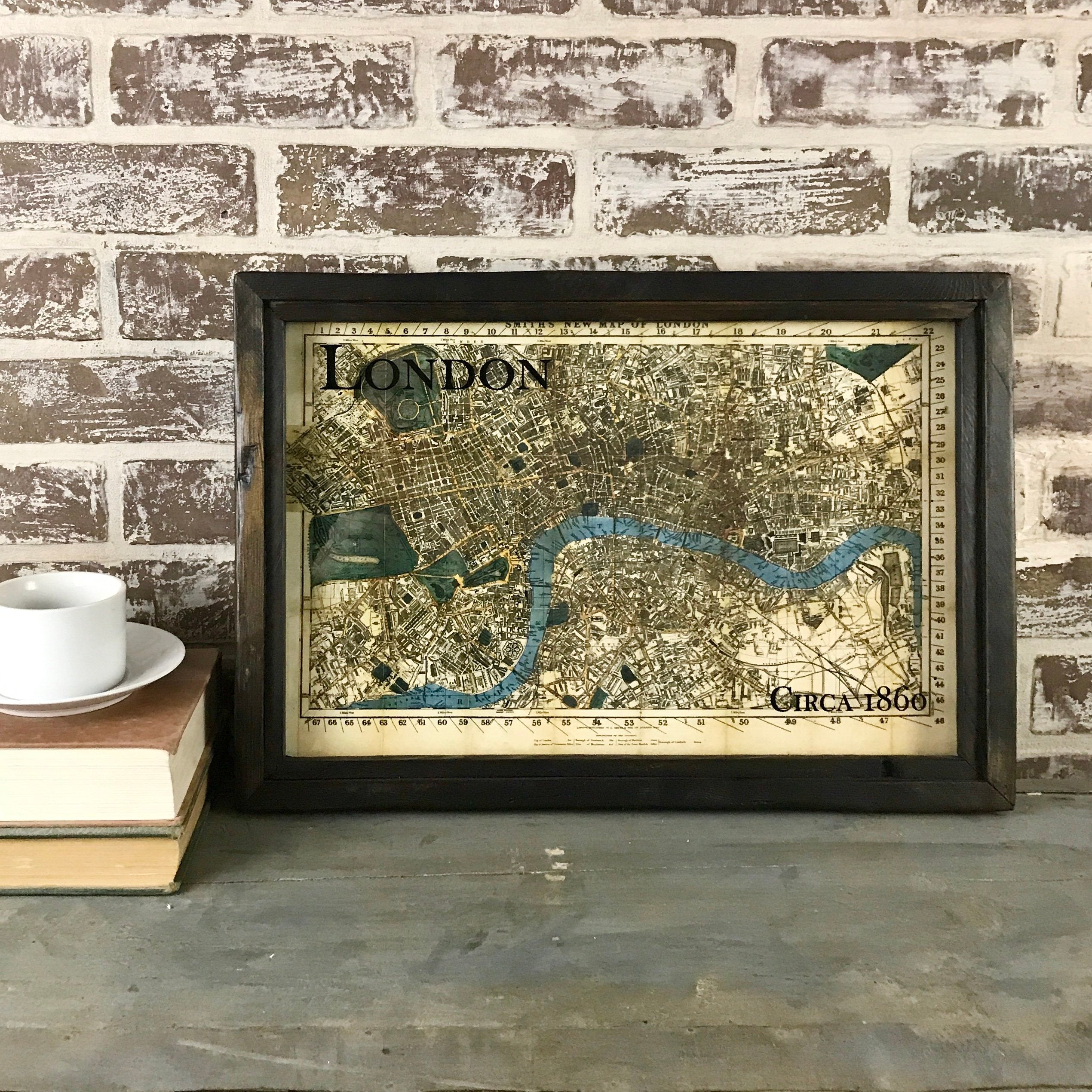 A framed map of London from 1860, displayed on a table with a cup and books in the background, with the word 'LONDON' visible on the map.