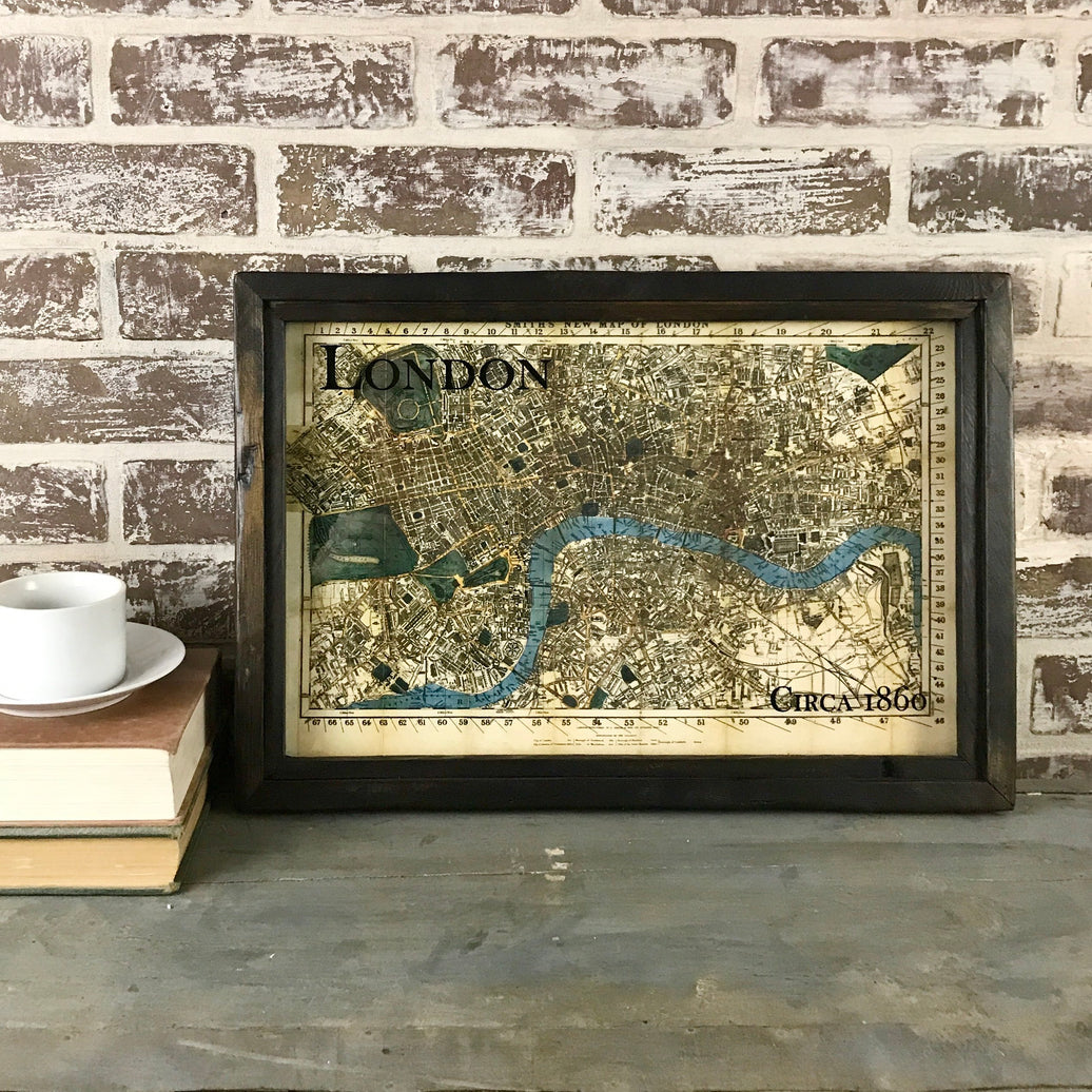 A framed map of London from 1860, displayed on a table with a cup and books in the background, with the word 'LONDON' visible on the map.