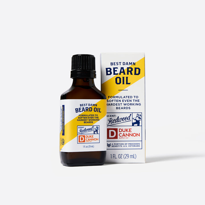 A bottle of Duke Cannon Beard Oil next to its packaging with branding and product information displayed on the front.