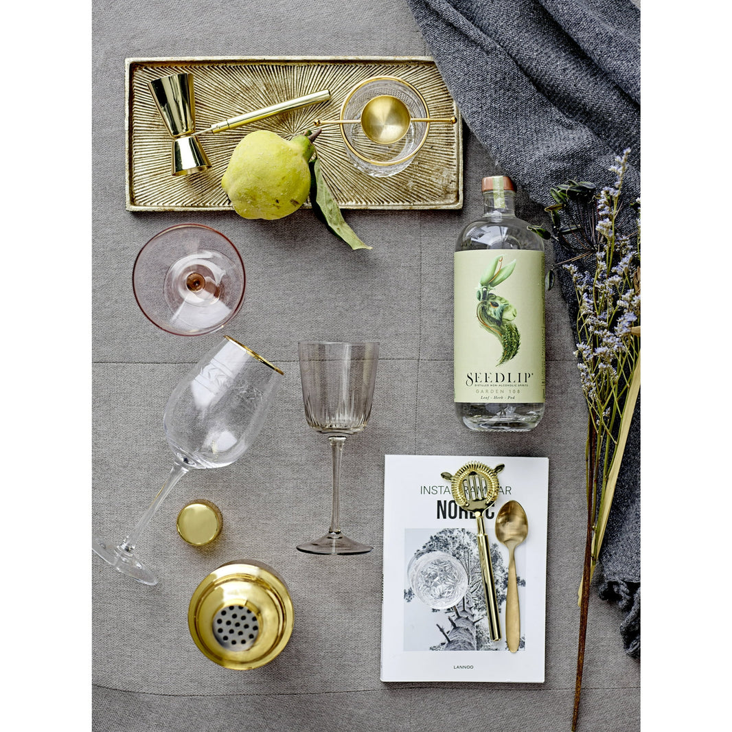 Bottle of Seedlip non-alcoholic spirit with glasses, a tray, and decorative elements on a gray surface.