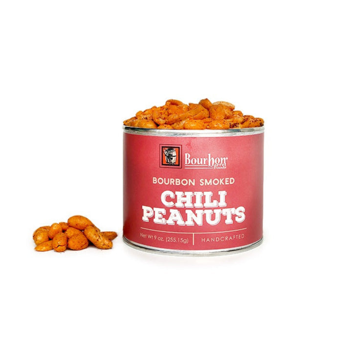 A red container of bourbon smoked chili peanuts with a few peanuts beside it on a white background.