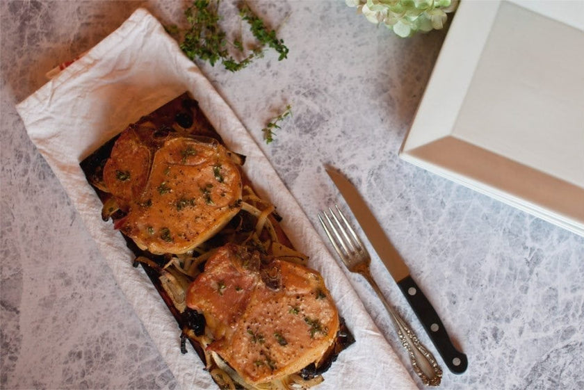 Grilled pork slices on a wooden grilling plank with a knife and fork.