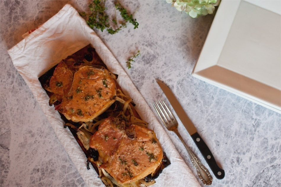Grilled pork slices on a wooden grilling plank with a knife and fork.