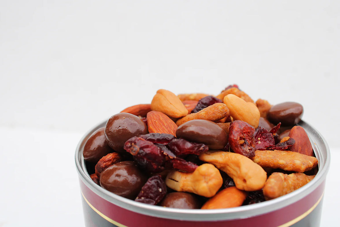 Assorted nuts and dried fruits in a metal tin on a white background