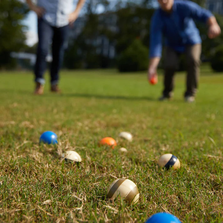 Colorful bocce balls on grass with people about to play in the background