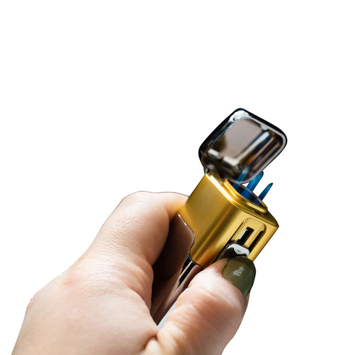A hand holding a gold accented butane cigar lighter with the flame active.