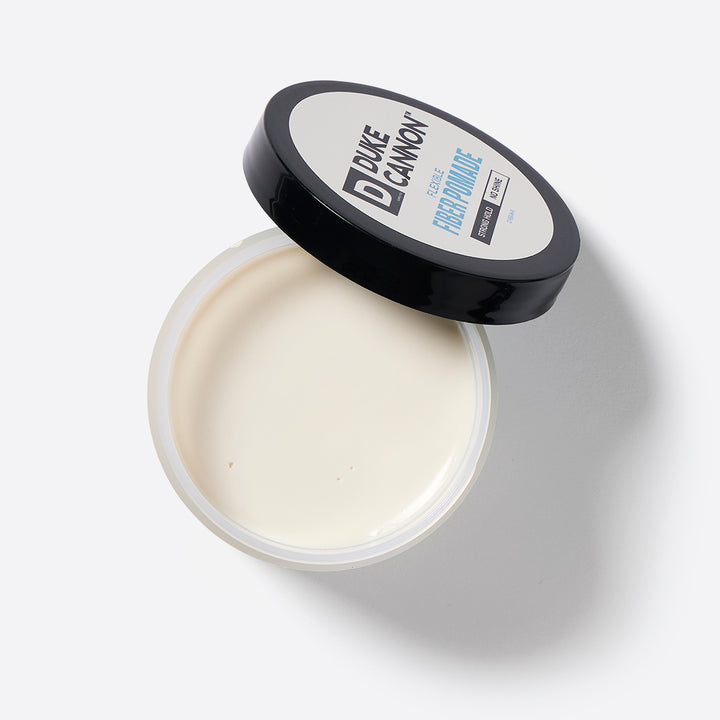A container of Duke Cannon Flexible Fiber Pomade with the lid open, showing the white pomade inside.