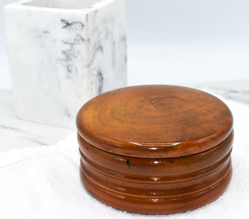 A honey-colored mango wood shaving bowl on a white towel next to marble bathroom items.