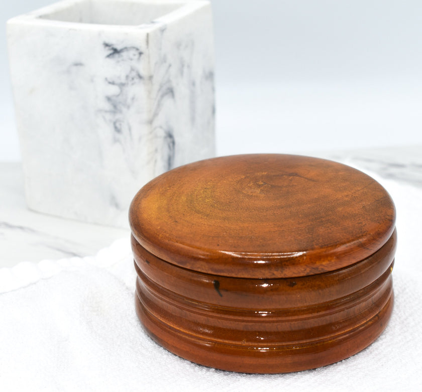 A honey-colored mango wood shaving bowl on a white towel next to marble bathroom items.