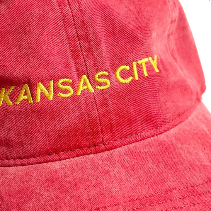 A close up of a red baseball cap embroidered with 'Kansas City' in gold thread.