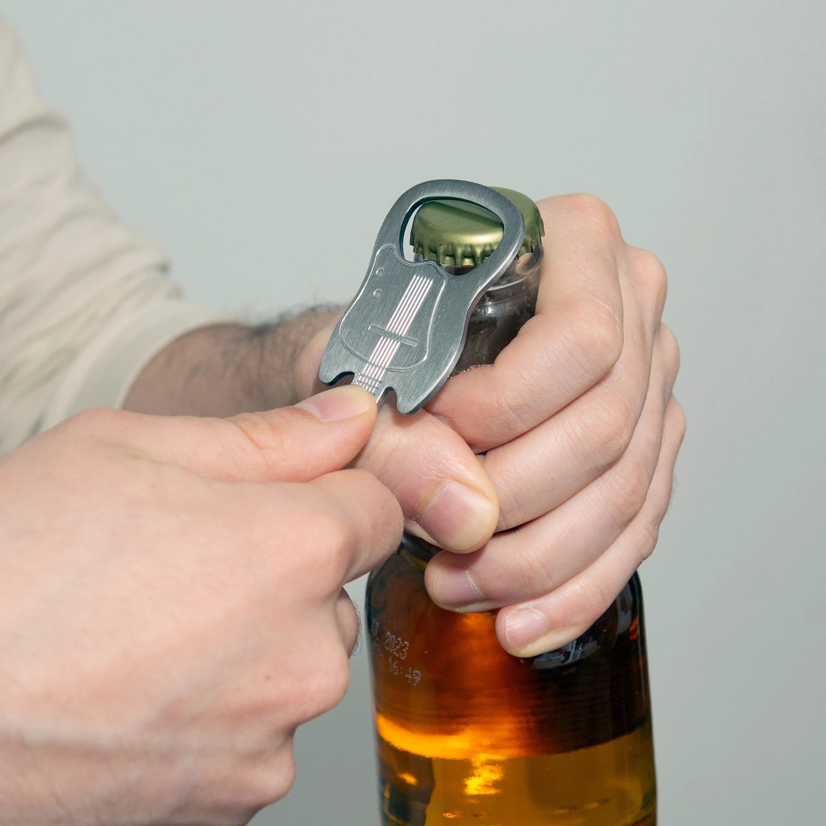 A person using a guitar shaped bottle opener on a bottle of beer.