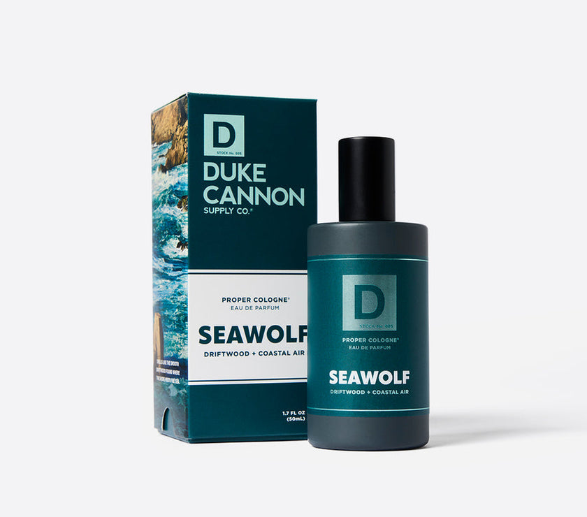 A product image featuring a bottle of Duke Cannon Proper Cologne - Seawolf next to its packaging box. The cologne bottle is dark blue with a black cap, and the box has a blue and green design with text and wave graphics.