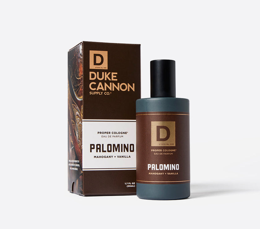 Packaging and bottle of Duke Cannon Proper Cologne in the scent 'Palomino'. The product is packaged in a brown box with the brand and product name, and a bottle with a dark cap and label displaying the same branding and scent name.