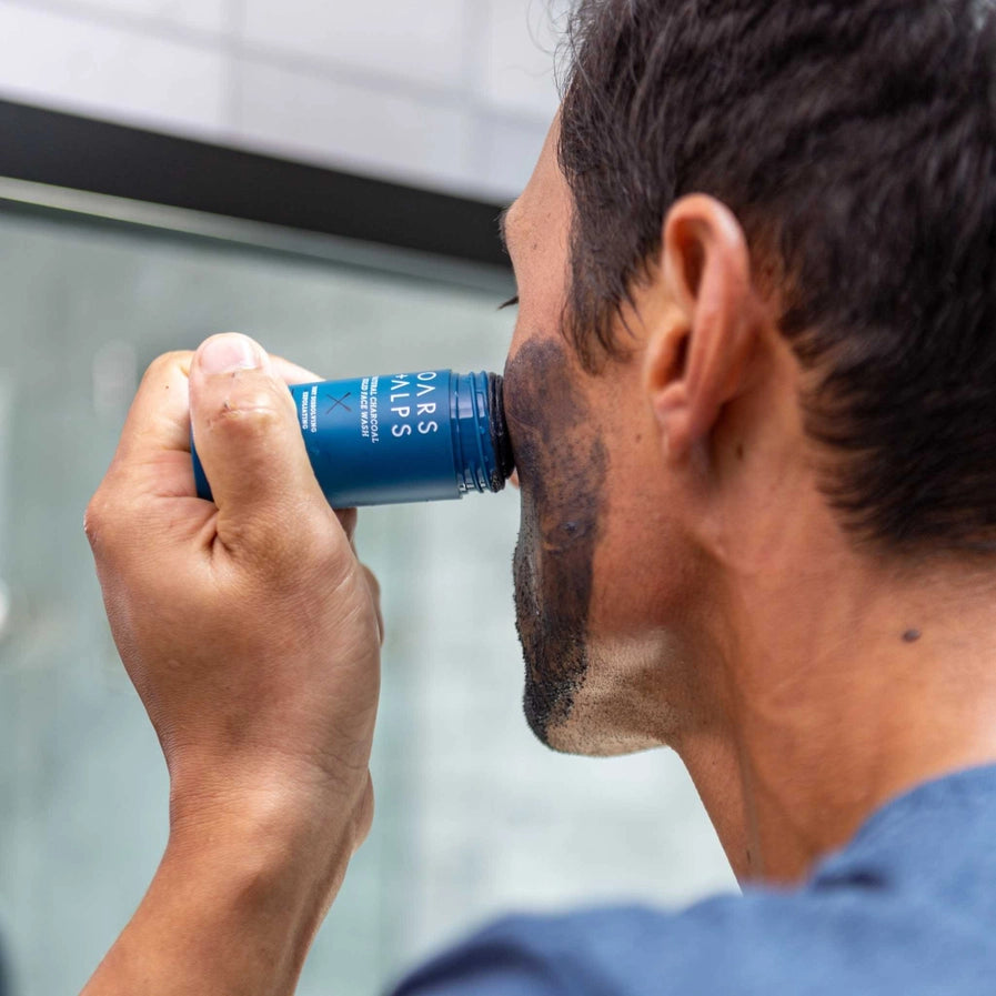 A man using the Oars + Alps Charcoal Exfoliating Solid Face Wash on his cheek.