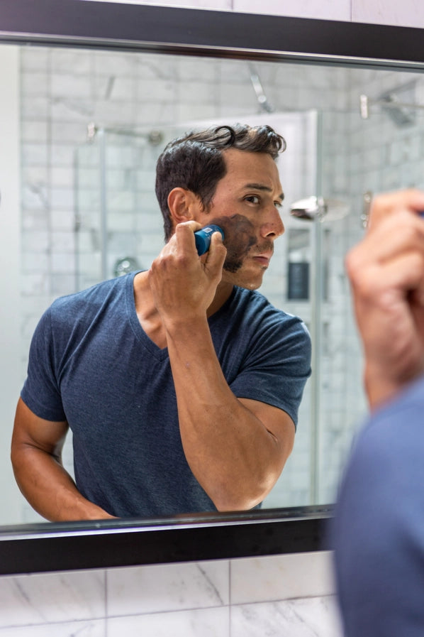 A man looking in the mirror as he uses the Oars + Alps Exfoliating Charcoal Face Wash.