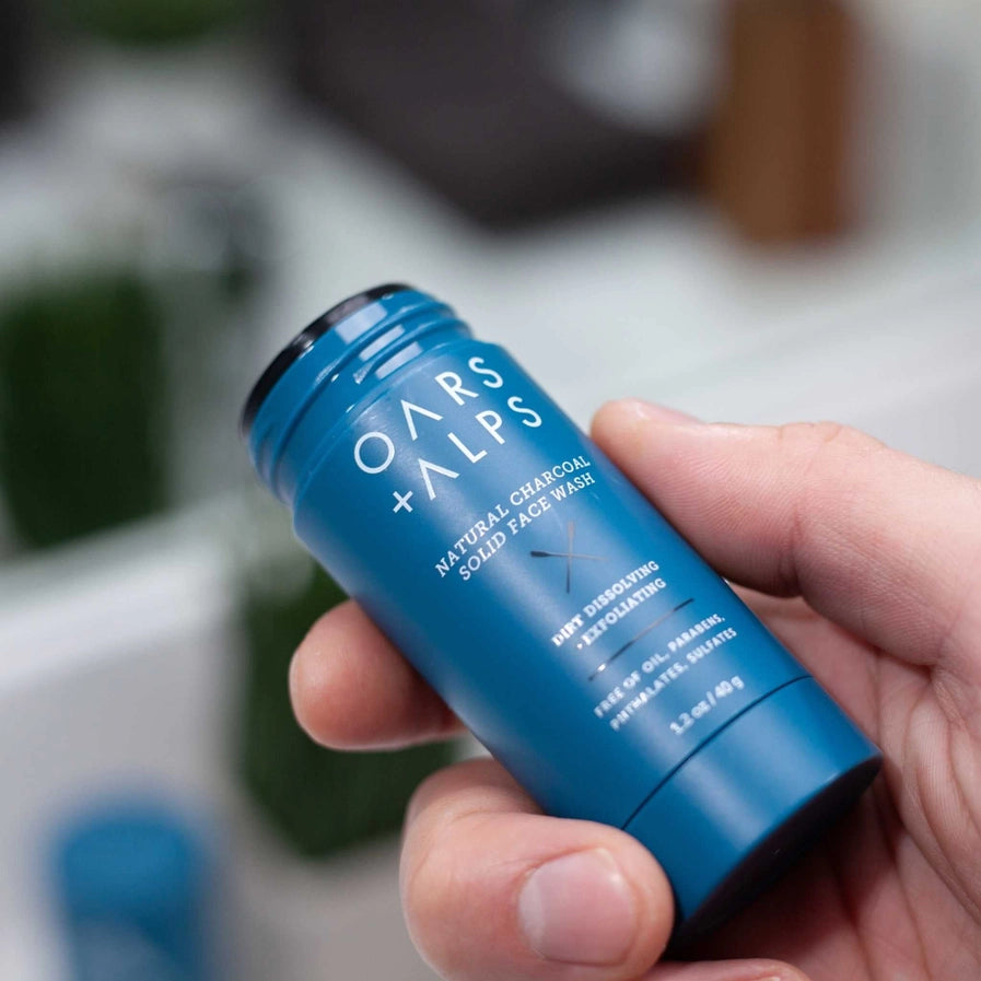 A person holding a container of the Oars + Alps Natural Charcoal Solid Face Wash.