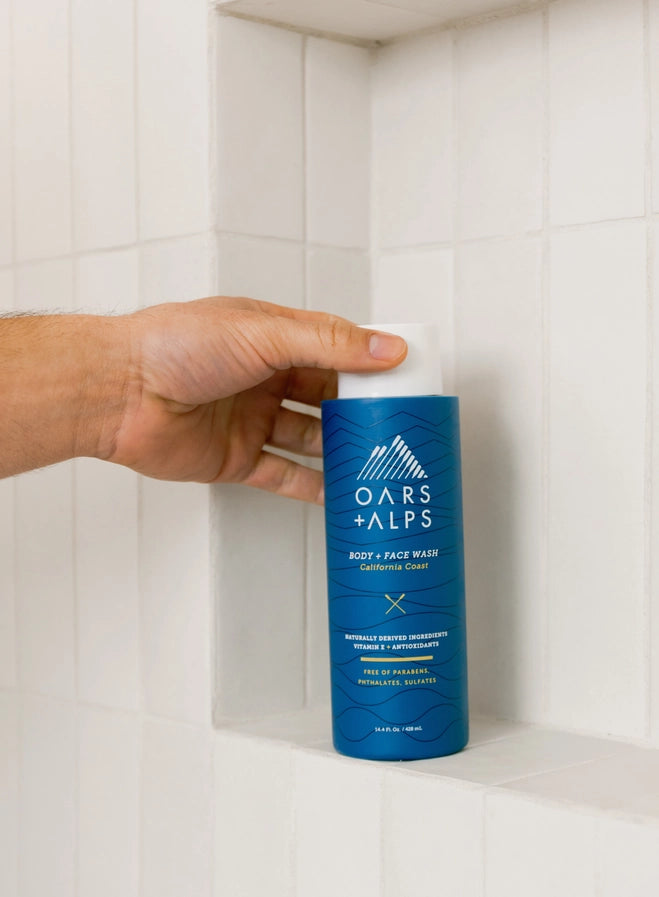 A hand holding the cap of the Oars + Alps Men's Body Wash.