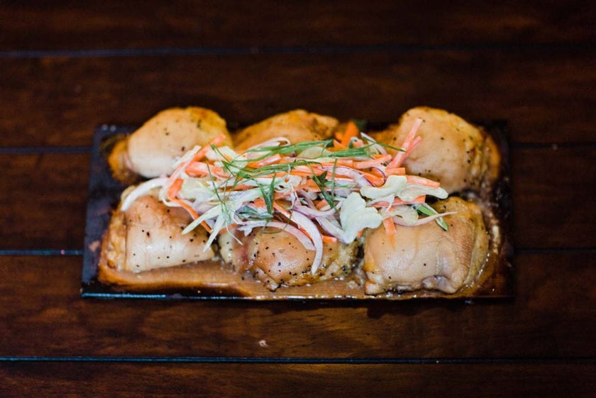 Grilled chicken thighs topped with coleslaw on a wooden grilling plank