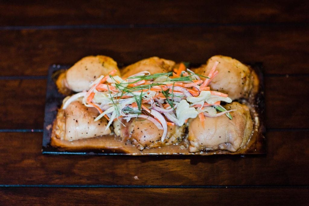 Grilled chicken thighs topped with coleslaw on a wooden grilling plank