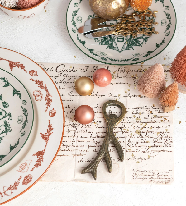 Decorative bottle opener with antler design on a table setting with ornamental plates, baubles, and little faux pine trees in pastel colors