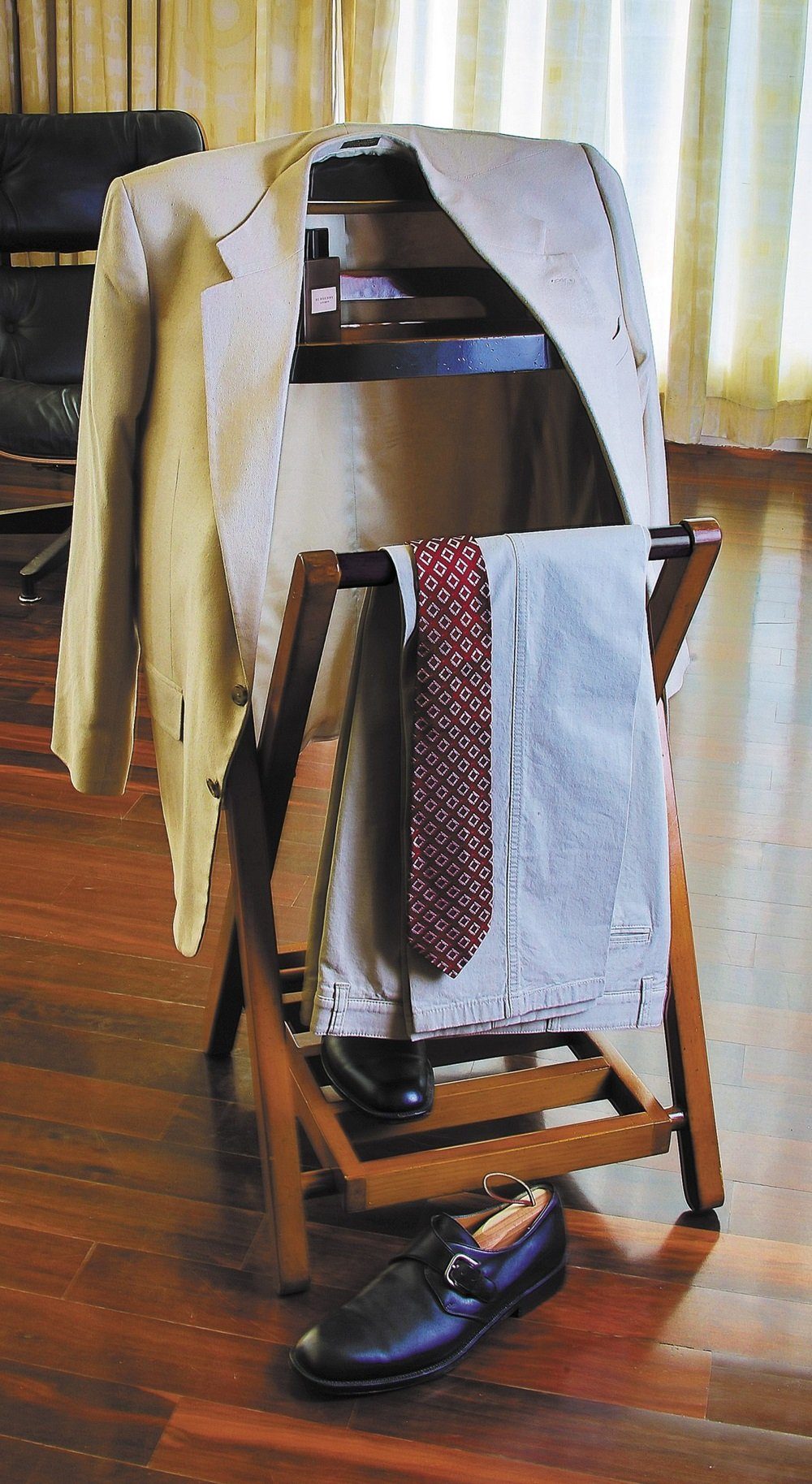 Wooden clothing rack with a beige jacket, patterned tie, and black shoes on a wooden floor.