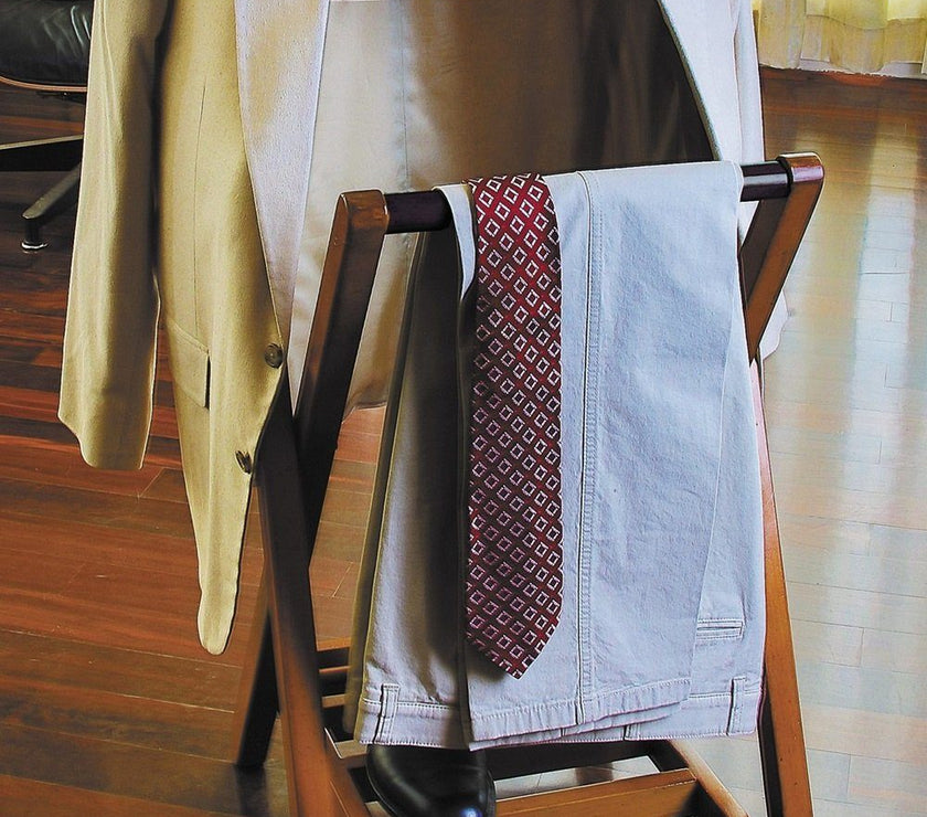 Wooden clothing rack with a beige jacket, patterned tie, and black shoes on a wooden floor.