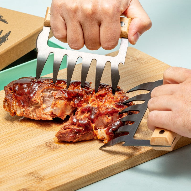 Person using meat shredding claws on barbecue chicken on a wooden cutting board