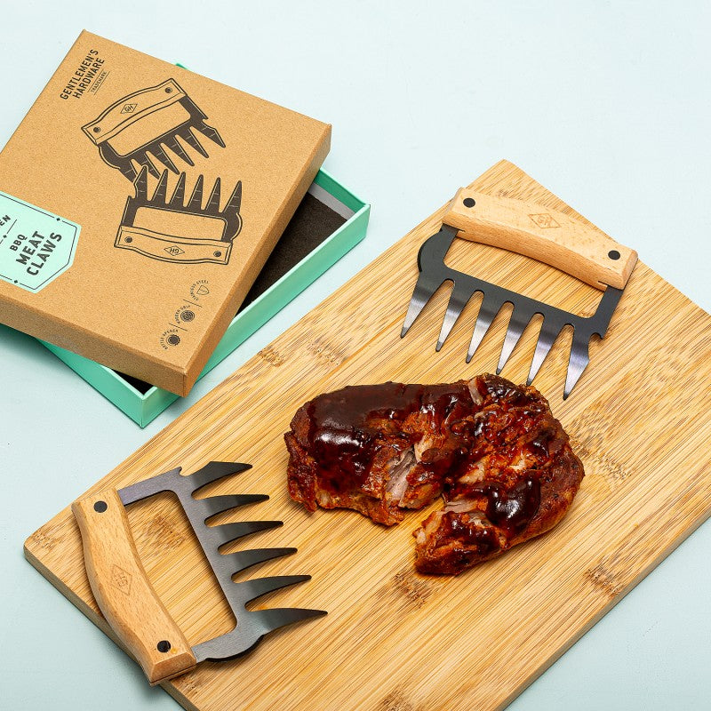 Two meat claws on a wooden cutting board with a piece of meat and a branded box in the background.