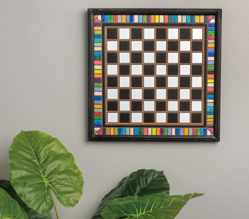 Framed checkered board with colorful border on a gray wall with a plant with green leaves below.