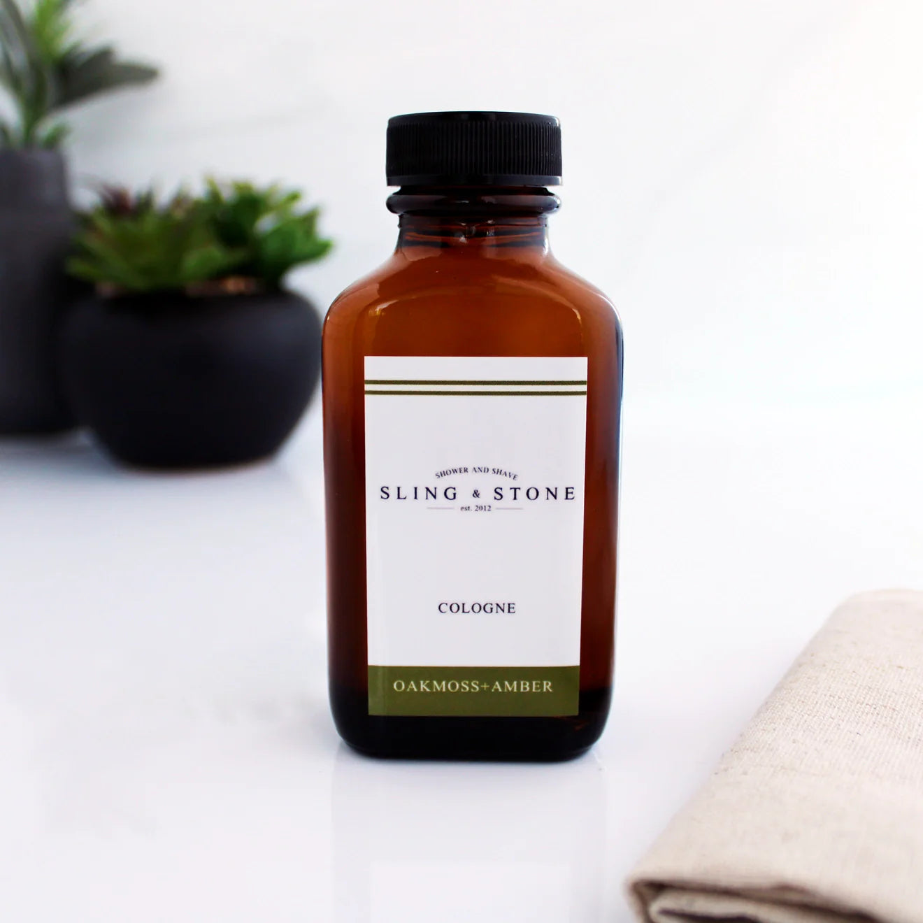 Brown bottle of Sling & Stone cologne with a label on a white surface.