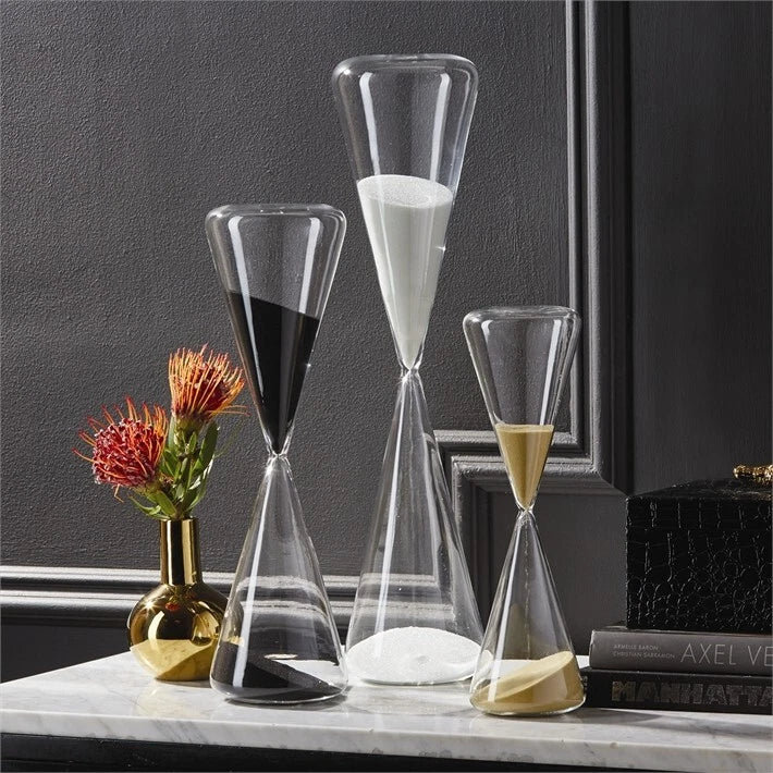 Three hourglass-shaped glass containers with different colored sands on a marble surface.