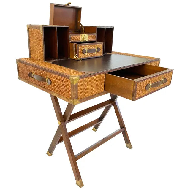 A traditional style campaign desk with a wicker and leather surface, with all of its drawers and compartments opened, standing on wooden legs.